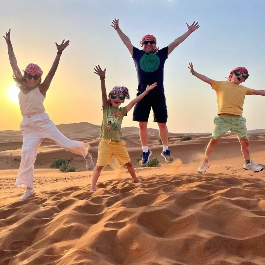 A family on a camel walk in the Sahara at sunset